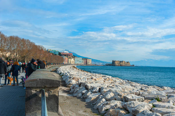 Naples, Italy - January 21, 2017: People strolling the Lungomare Caracciolo,  romantic seaside promenade with views of Naples, castles & Mt. Vesuvius