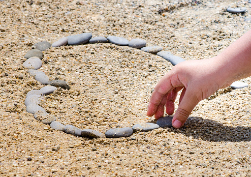 child lays out a heart from stones on a sandy beach
