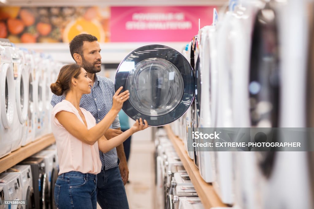 Young couple looking for a proper drying machine Young couple seen in a home appliances store in front of a drying machine. Appliance Stock Photo