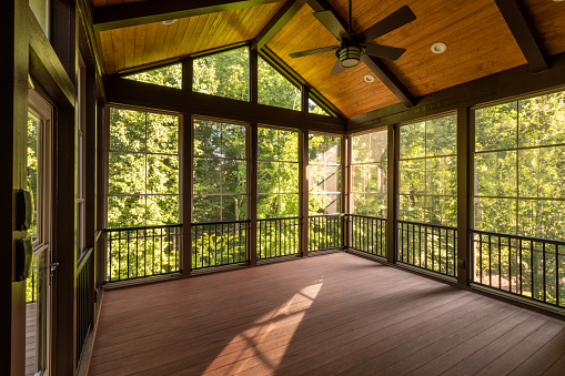 Modern screened porch enclosure with plastic windows and composite floor with summer woods in the background.