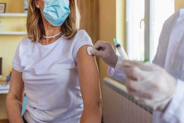istock Close up of general practitioner hand holding vaccine injection while wearing face protective mask during covid-19 pandemic. Mature man nurse with surgical mask giving injection to senior woman. 1329394460