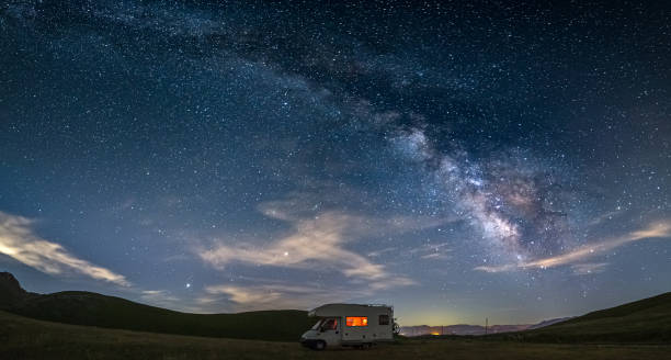 istock Panoramic night sky over Campo Imperatore highlands, Abruzzo, Italy. The Milky Way galaxy arc and stars over illuminated camper van. Camping freedom in unique hills landscape. 1329397005