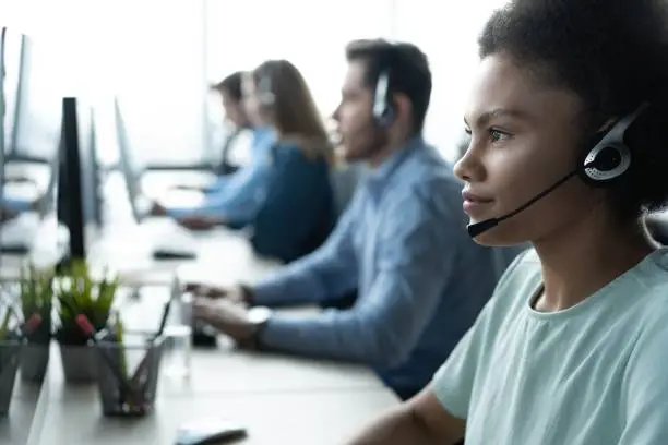 Photo of How can I help you? Beautiful call center workers in headphones are working at modern office