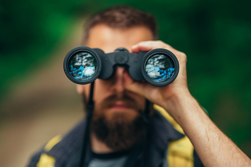 Young man hiker walking in forest using binoculars