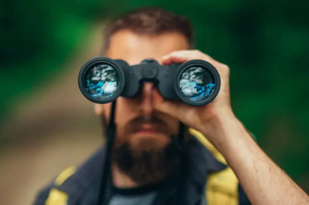 Photo of Binoculars being used by a male hiker while spending time in the nature