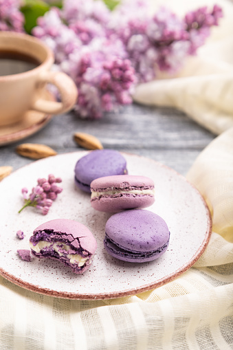 Purple macarons or macaroons cakes with cup of coffee on a gray wooden background and white linen textile. Side view, close up, selective focus.