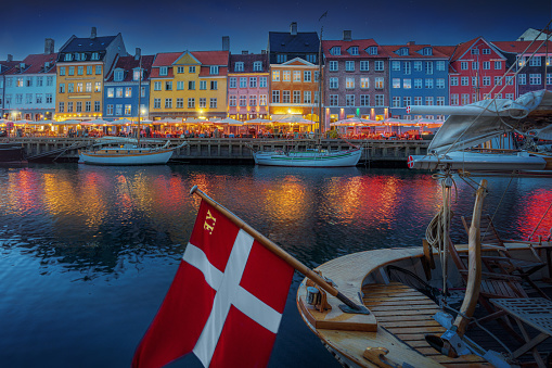 Illuminated view of Nyhavn port and waterfront at night with the flag of Denmark - Copenhagen, Denmark