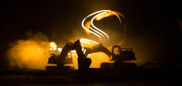 istock Construction site on a city street. A yellow digger excavator parked during the night on a construction site. Industrial concept table decoration on dark foggy toned background. 1329408857