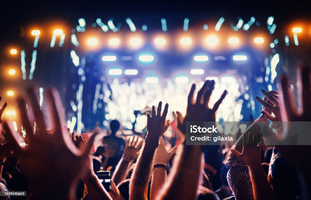 Large group of people at a concert party. Rear view of large group of people enjoying a concert performance. There are many raised hands in front of the camera. Music Festival Stock Photo