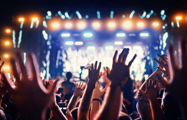 Large group of people at a concert party. Rear view of large group of people enjoying a concert performance. There are many raised hands in front of the camera. performing arts event stock pictures, royalty-free photos & images