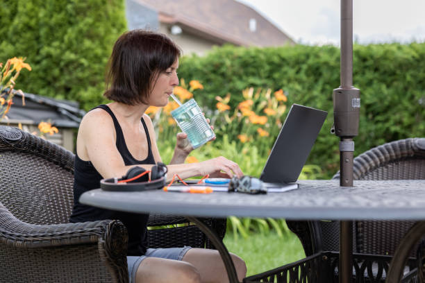 mujer usando una computadora portátil y trabajando desde casa al aire libre en su patio trasero - shirt women isolated camisole fotografías e imágenes de stock