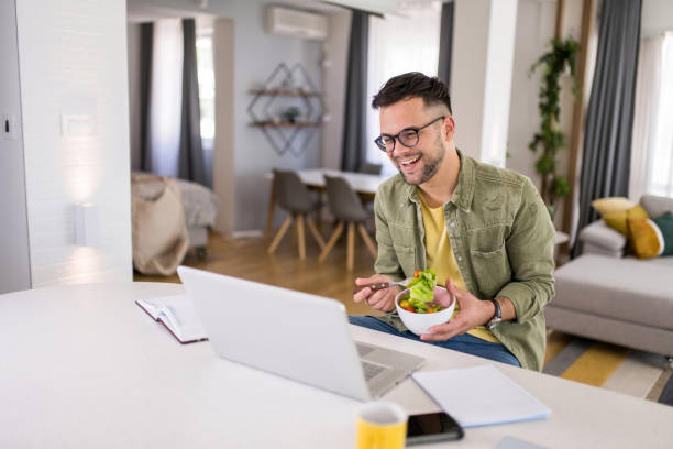 istock Young man eating a salad while working in comfort of his home. 1329420672