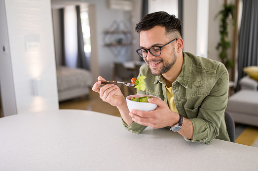 Happy young man eating a healthy salad for breakfast in the living room.
