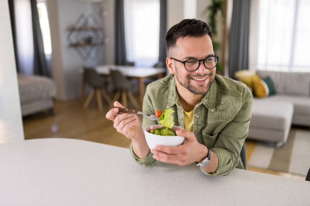 istock Young man eating a salad at home. 1329420809