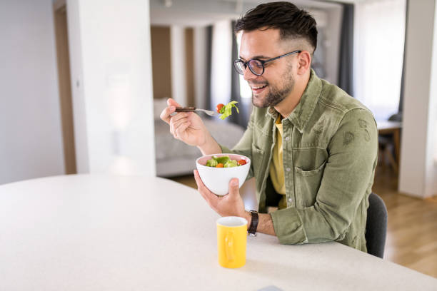 istock Young man eating a salad at home. 1329420851