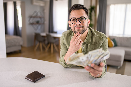 Young male entrepreneur sitting at home with a lot of cash and thinking of a way to spend it wisely.