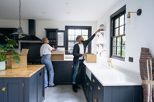 Full length view of mid adult man and woman in casual clothing placing glasses in cabinets and jars on shelves on moving day.