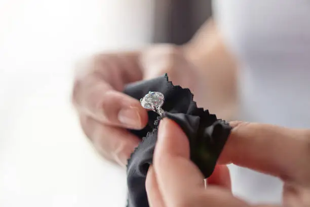 Photo of Jeweller cleaning jewelry diamond ring with fabric cloth