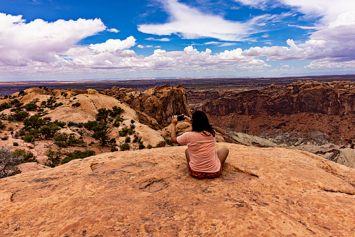Young adult takes a video with her smart phone of the deep crater in front of her at the Upheaval Dome Overlook in Canyonlands near Moab, Utah
