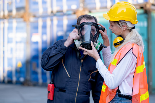 Cargo container woman worker help technician to wear gas protective mask and prepare for manage the problem in workplace area.