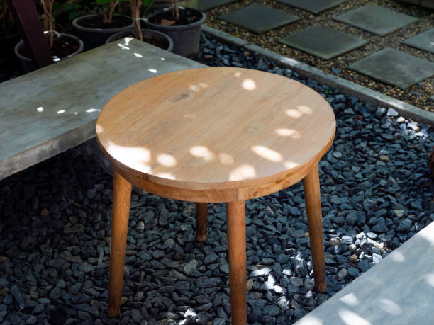 Empty round wooden side table with simple cement seat on gravel floor near the walkway in the backyard garden, top view.