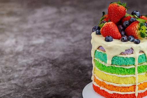 Close up of rainbow birthday cake decorated with fresh berries.