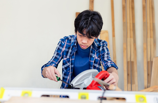 Young carpenter using a screwdriver fixing circular saw in carpentry workshop, Child learning woodworking in the craftsman workshop