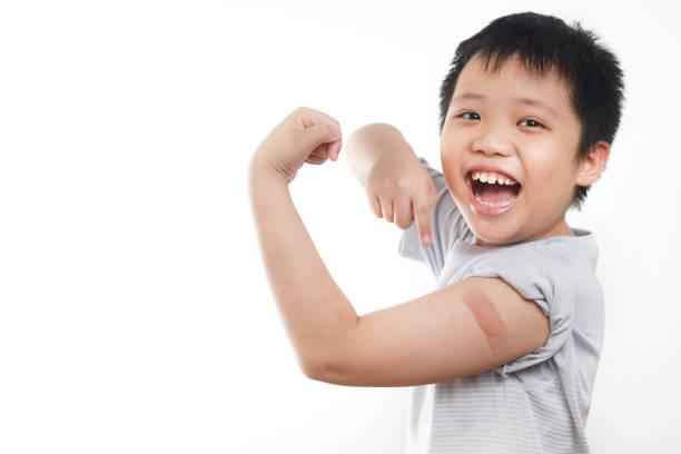 Portrait of happy Asian boy get vaccinated, showing his shoulder with band-aid after getting a vaccine. stock photo