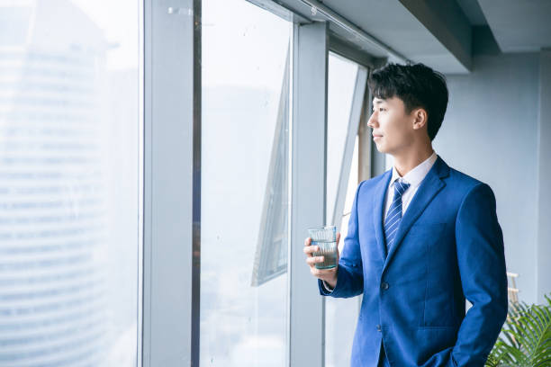 istock Businessman holding cup water standing by office window 1329442947