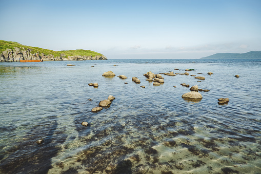 summer sea panorama. shallow, clear, transparent sea with reefs, rocks and green hills around. Japan sea.