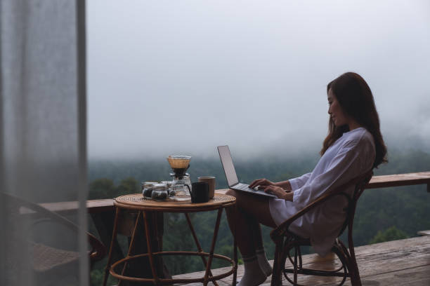 istock A young asian woman using and working on laptop computer while sitting on balcony with a beautiful nature view on foggy day 1329445602