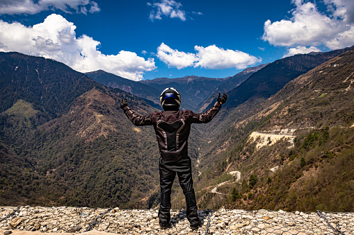 biker wearing safety gears at mountain top with bright blue sky at day image is taken at sela pass tawang arunachal pradesh india.
