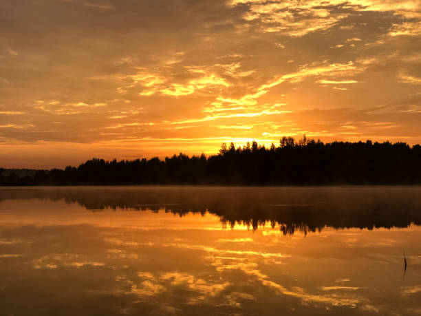 istock Dramatic orange sky at sunset over forest lake reflecting on still water surface, forest line silhouetted on horizon 1329446444
