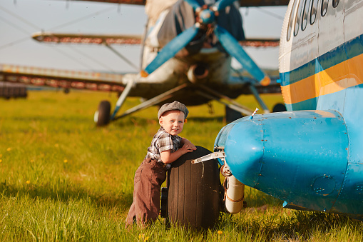 A cute little boy stands next to the propeller of an old airplane on a Sunny day