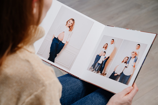 top view. woman watches photobook from photo shoot of family. storage of photos in photo album. work of designer, photographer and printer. memory of important moments of life
