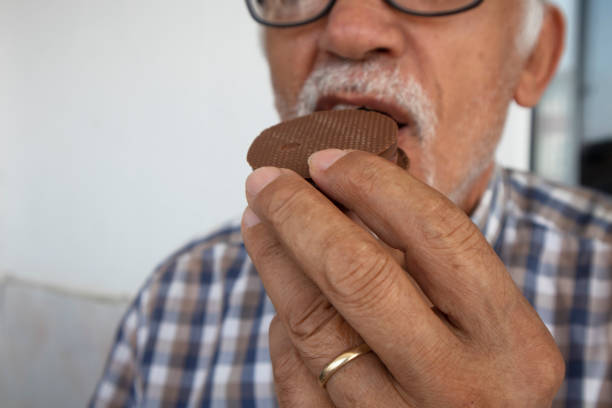 Elderly man eating chocolate cookie. The concept of enjoying life in retirement