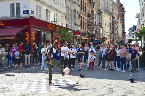 Brussels, Belgium - July 17, 2021: African young adult playing tricks with football in the middle of the street to earn some money from the tourists.