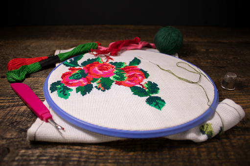 Embroidery and embroidery accessories.The canvas is put on an embroidery frame,embroidery threads and a thimble with a rasparyvatel.The photo is made on a wooden background.