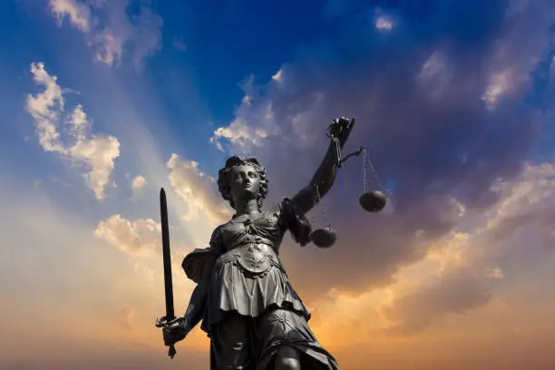 Lady justice at the Roemer in Frankfurt am Main symbolizes Justice with sword and scales under dramatic sky.