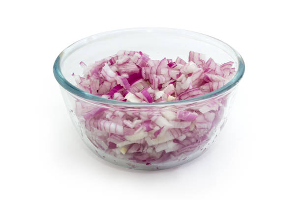 Finely chopped red onion in the glass transparent bowl on a white background, selective focus