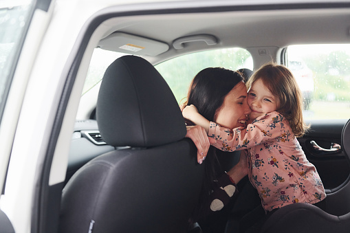 Embracing each other. Mother with her daughter inside of modern automobile together.