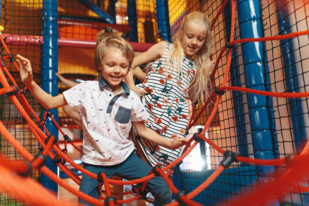 happy group of siblings playing together on indoor playground. excited kids playing together on net ropes. cute school kids playing on colorful playground at shopping mall - playground schoolyard playful playing imagens e fotografias de stock