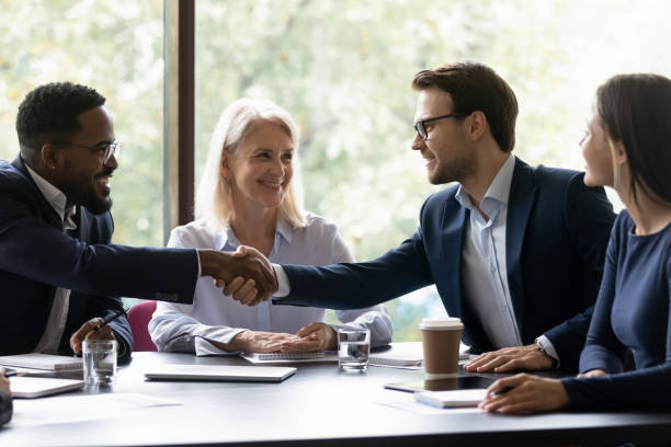 istock Happy diverse business partners shaking hands over table 1329476180
