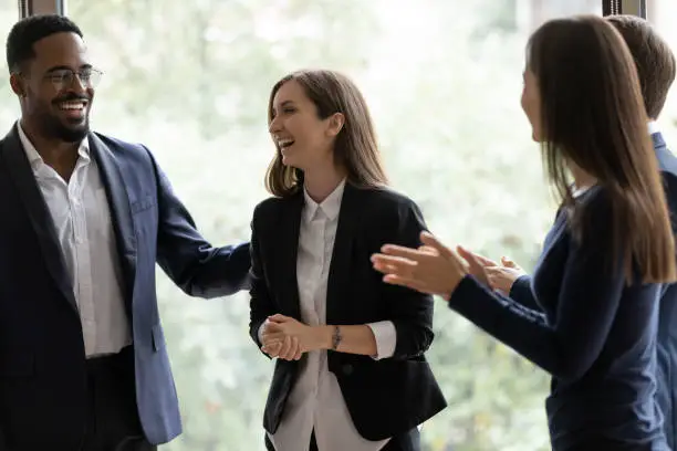 Photo of Happy diverse business team applauding coworker success