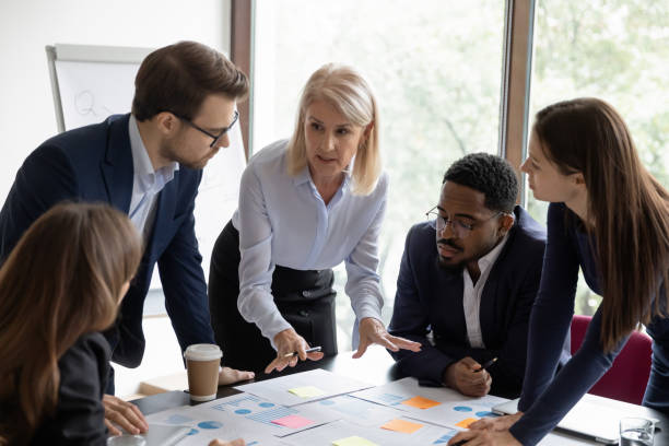 Mature business teacher training group of employees Mature business teacher training group of employees, teaching to work with paper reports, analyze marketing charts, using sticky notes. Mentor explaining scrum method tools to employees scrum stock pictures, royalty-free photos & images