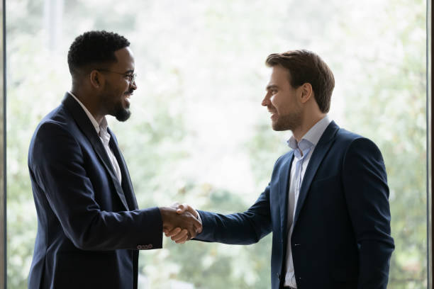 istock Two diverse businessmen, business partners shaking hands at window 1329476215