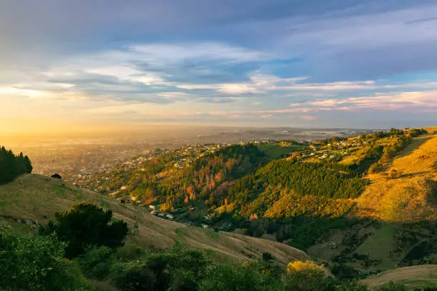 This June 2021 sunset image shows Ōtautahi Christchurch, Aotearoa New Zealand as viewed from Victoria Park in the Port Hills. The city is the largest on Te Waipounamu South Island. The farmland of Horomaka Banks Peninsula in the foreground quickly transitions into an urban area in the background. The Ōtākaro Avon Heathcote Estuary and the Pacific Ocean coastline are seen in the distance.