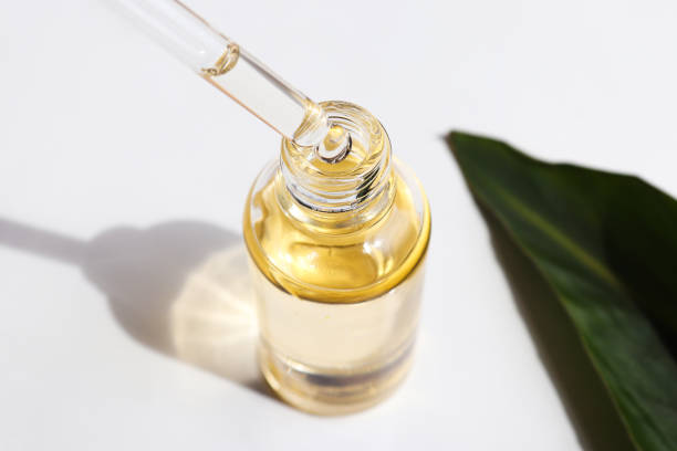 bottle of cosmetic essential oil and green leaf. serum oil is dripping from dropper. close-up. beauty and body care concept. serum skin care product. hard light - druppelfles stockfoto's en -beelden