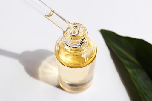 Bottle of cosmetic essential oil and green leaf. Serum oil is dripping from dropper. Close-up. Beauty and body care concept. Serum skin care product. Hard light.