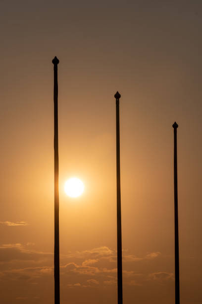 Helsinki / Finland - JULY 12, 2021: Silhouettes of tree tall flag poles against bright setting sun.